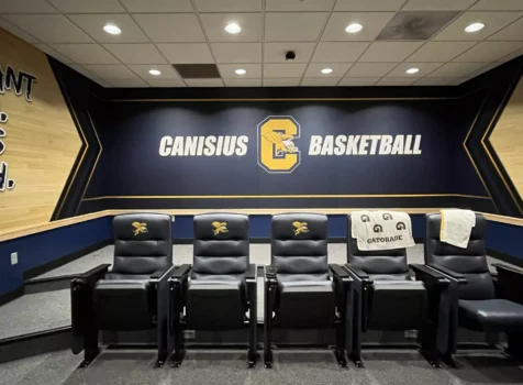 A media or film room for the Canisius College basketball team. The room features a dark blue and gold color scheme, with “CANISIUS BASKETBALL” displayed on the back wall alongside the team’s logo.