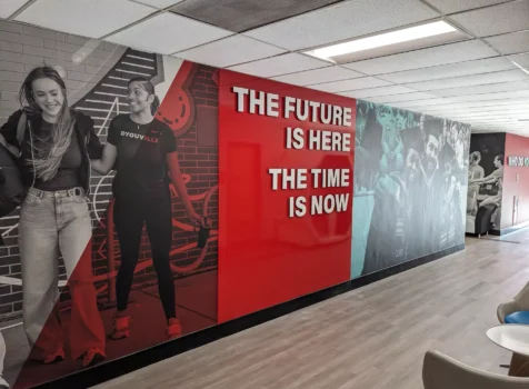 A modern hallway at D’Youville University featuring a large motivational wall mural. The mural is divided into sections with a mix of black-and-white and red-accented images.