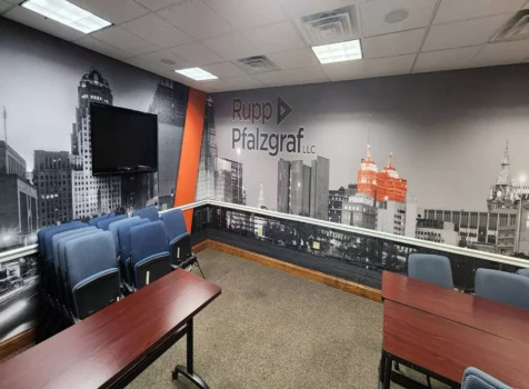 A conference room with a large black-and-white cityscape mural featuring selective color on certain buildings. The wall displays the “Rupp Pfalzgraf LLC” logo.